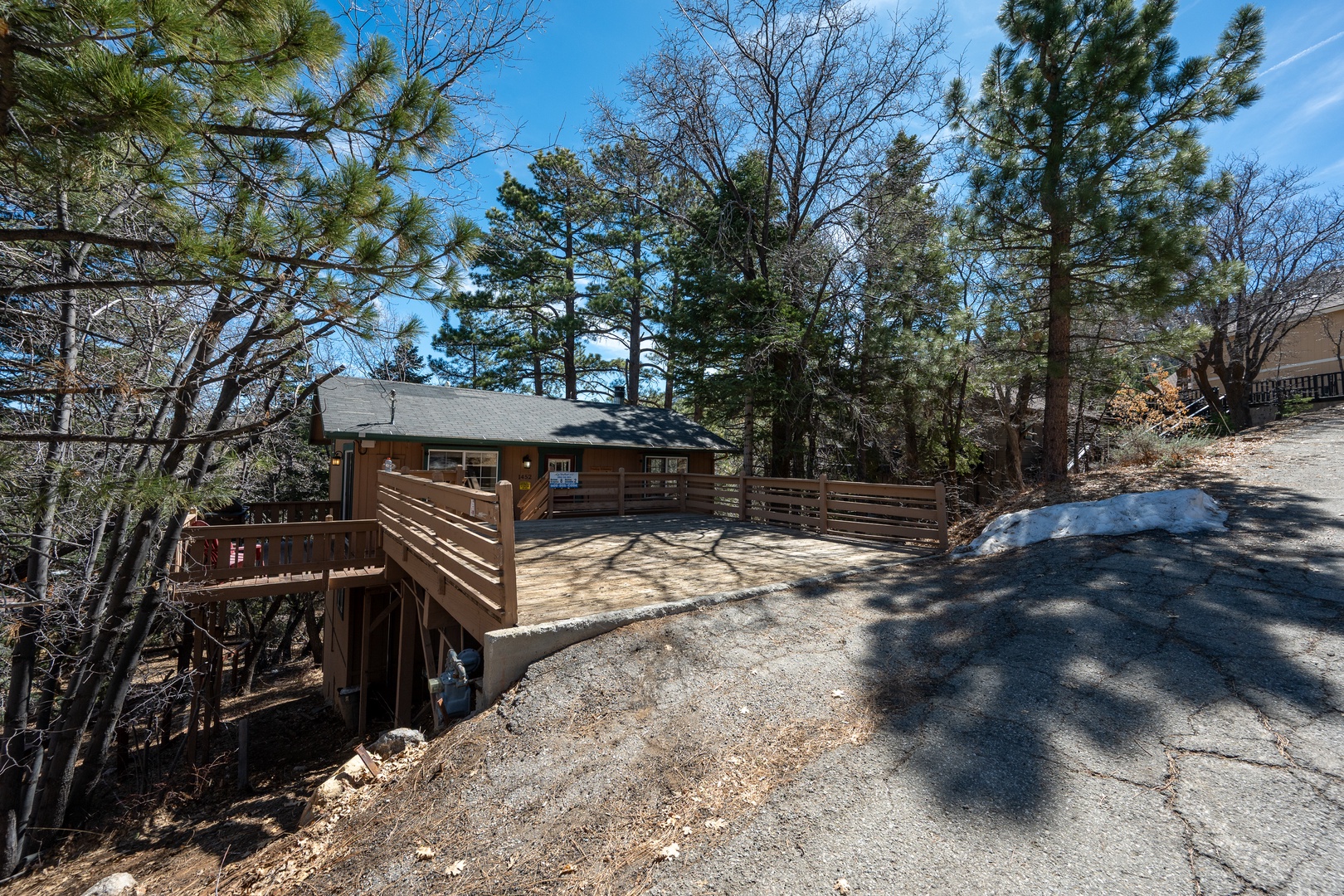 A charming mountain retreat nestled among tall pines with private parking and multi-level deck access, offering peaceful seclusion under bright blue skies.