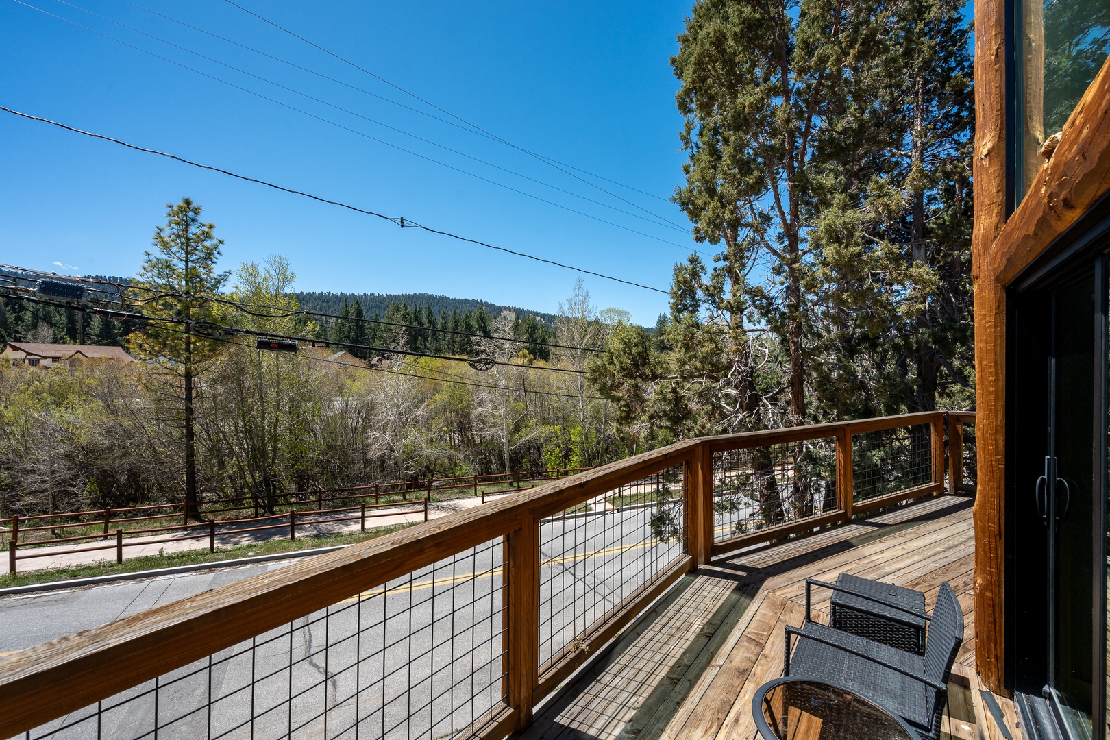 A peaceful street borders the property, framed by towering evergreens and rolling mountains under a clear blue sky, offering a scenic and tranquil mountain neighborhood setting.