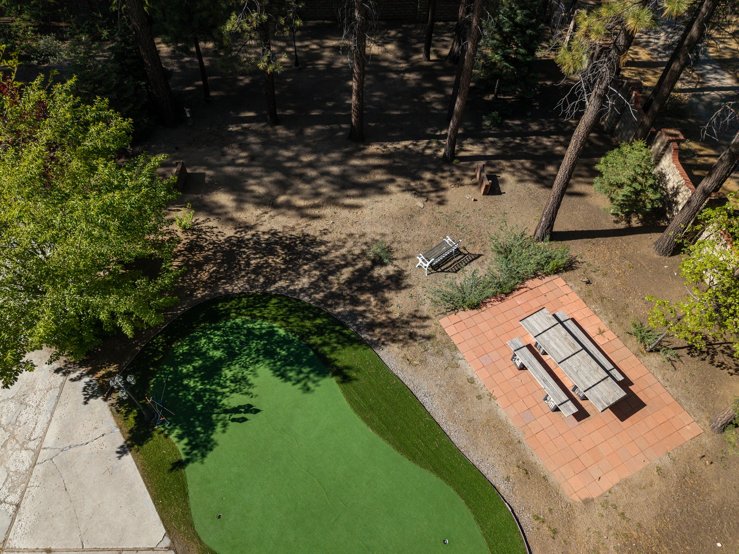 Aerial view of the property's recreational area featuring a miniature golf course, picnic patio with seating, and surrounding pine forest.