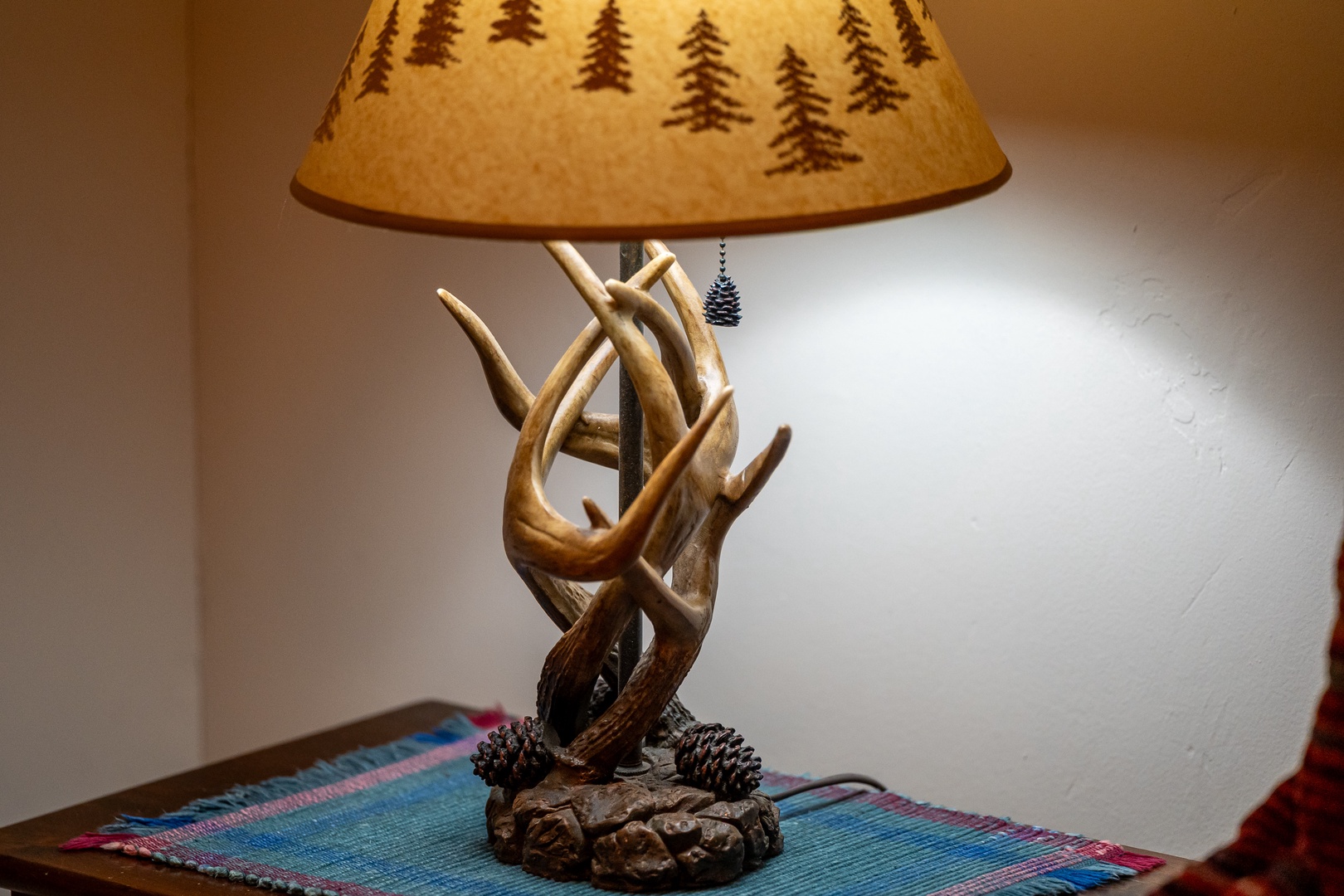 Cozy up by this rustic antler lamp with its charming pine tree shade, casting warm light perfect for your mountain retreat evenings.