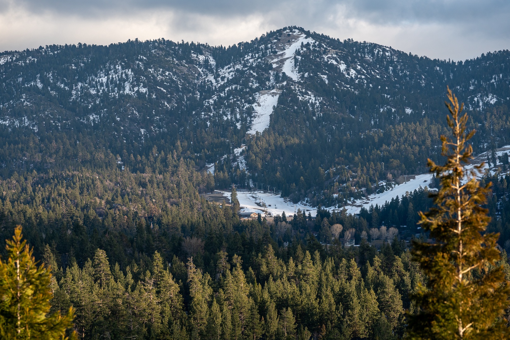 Snow-dusted mountains create a dramatic backdrop with visible ski slopes cutting through the forested peaks.