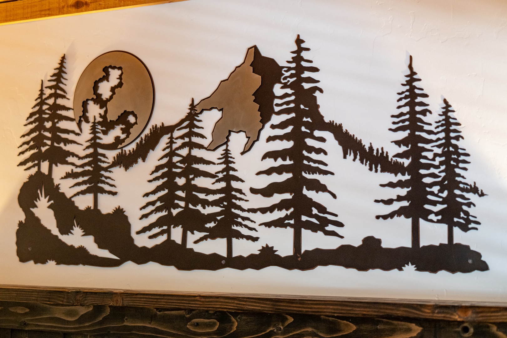 A metal silhouette depicts a wolf howling beneath a moon, surrounded by tall pines—wilderness art that celebrates the spirit of nature's untamed beauty.