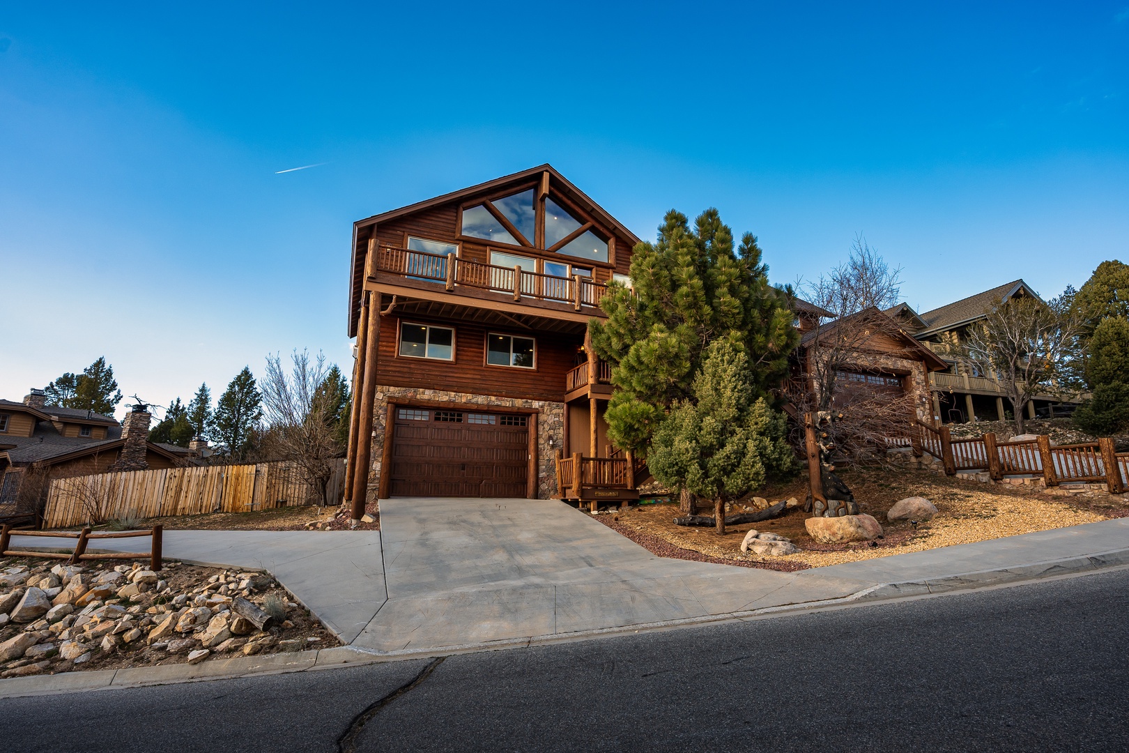 Modern mountain lodge featuring stone and wood architecture sits in established neighborhood with mature landscaping.