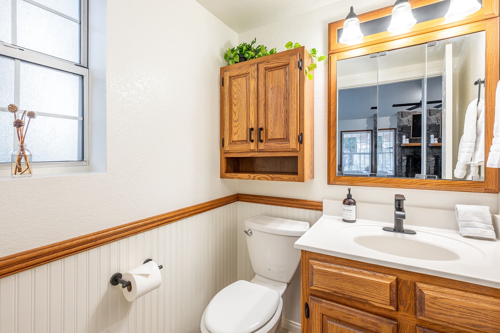 Your charming guest bathroom features warm oak cabinetry, crisp white fixtures, and natural light from the window creating a welcoming space for freshening up.