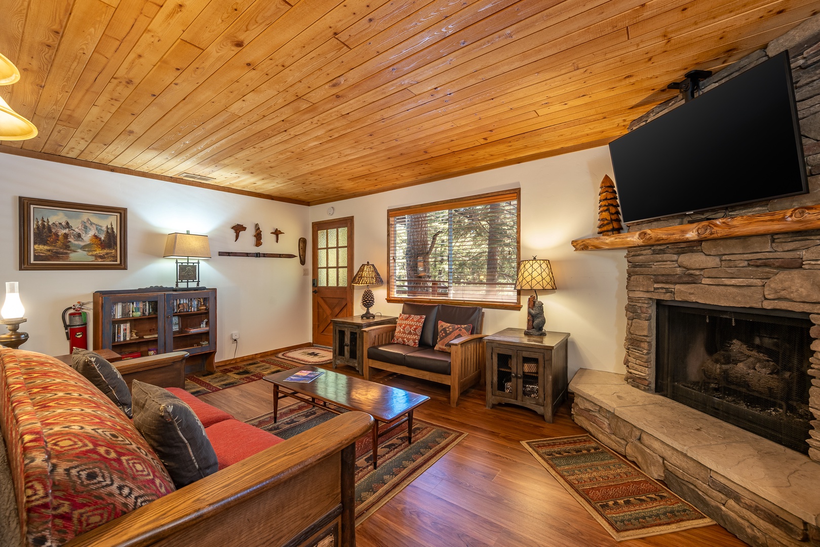 Curl up by the stone fireplace in your cozy living room, where rustic wood ceilings and mountain-cabin charm invite you to unwind after a day of adventure.