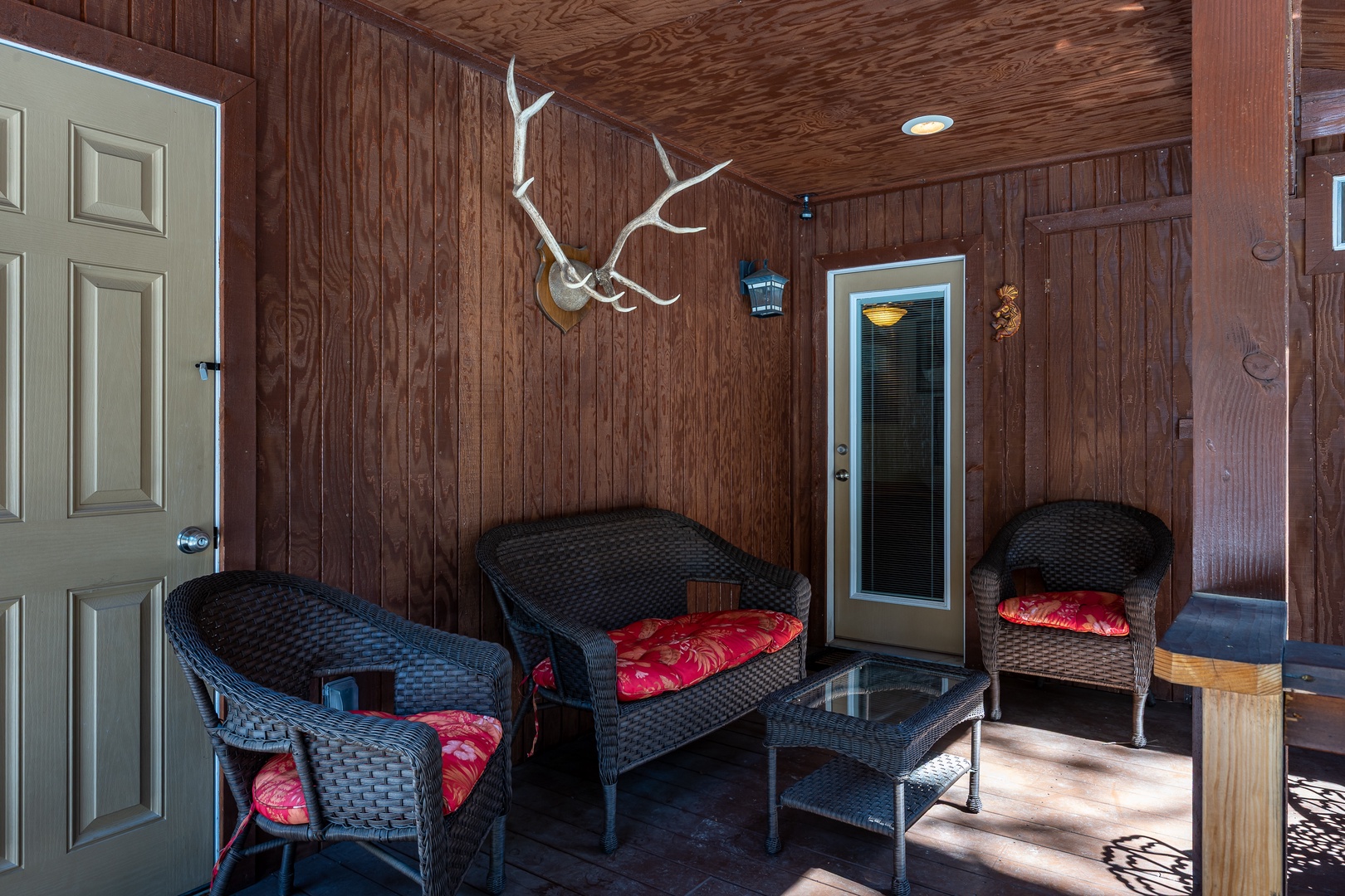 Relax on your private covered porch, where rustic charm meets comfort with wicker seating, bold red cushions, and a distinctive antler accent overhead.