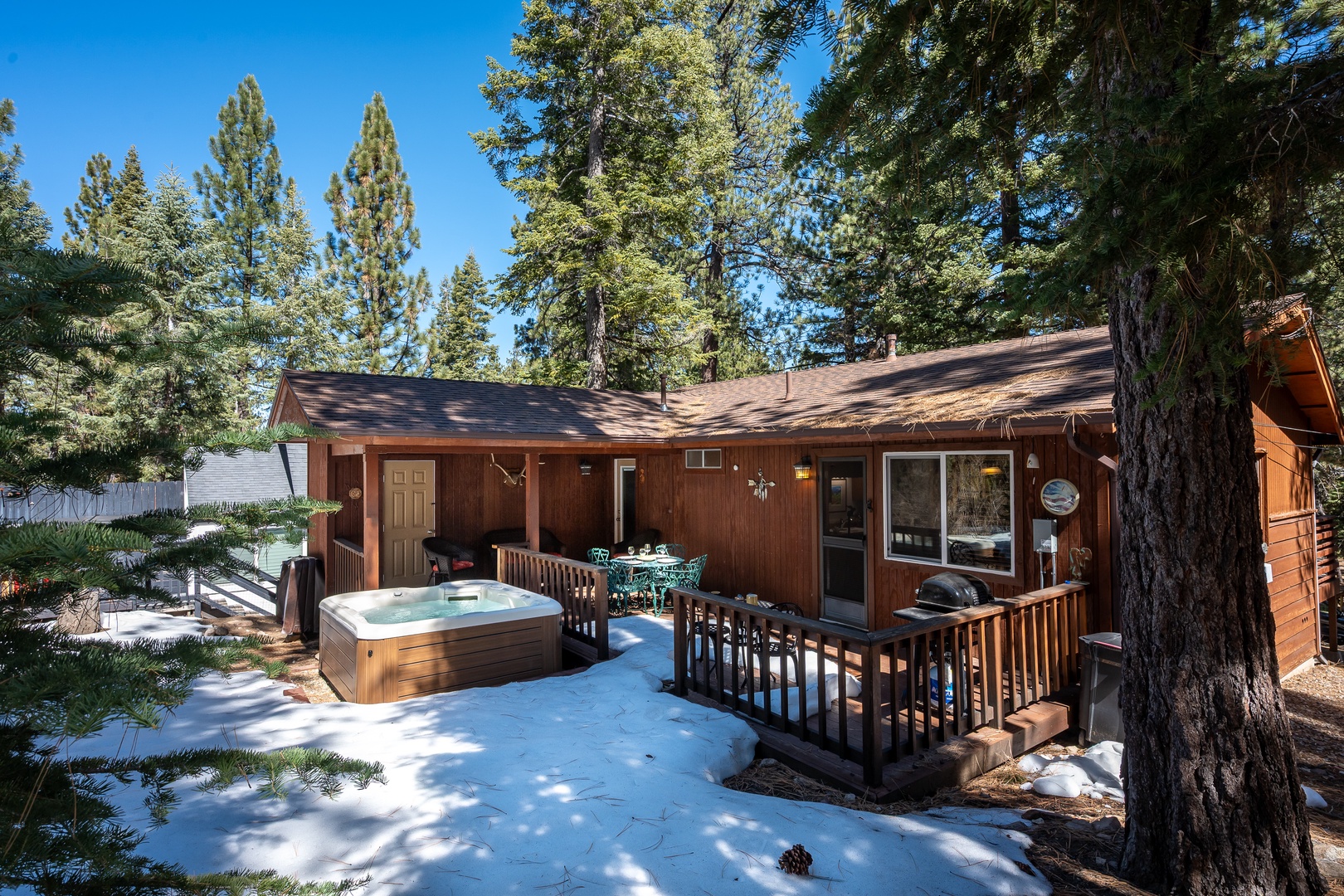 A cozy mountain cabin nestled among towering pines, featuring a private hot tub and deck area surrounded by pristine winter snow and forest beauty.