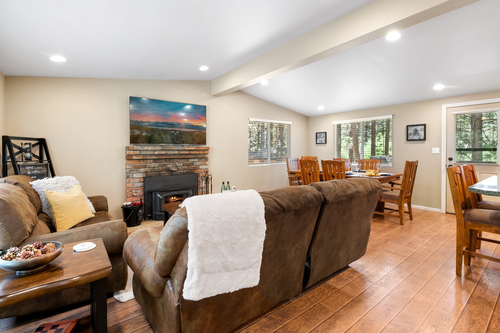 Sink into plush seating by the stone fireplace, enjoy meals at the large dining table, and gaze through windows framing peaceful forest views—your mountain retreat awaits.