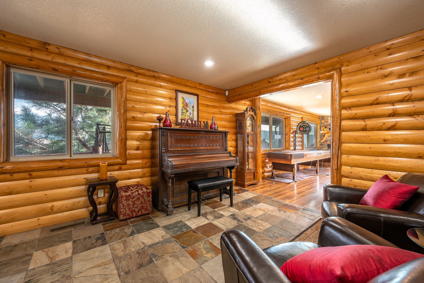 Cozy up in your rustic living room with warm log walls, leather seating, and a vintage piano for memorable evenings.