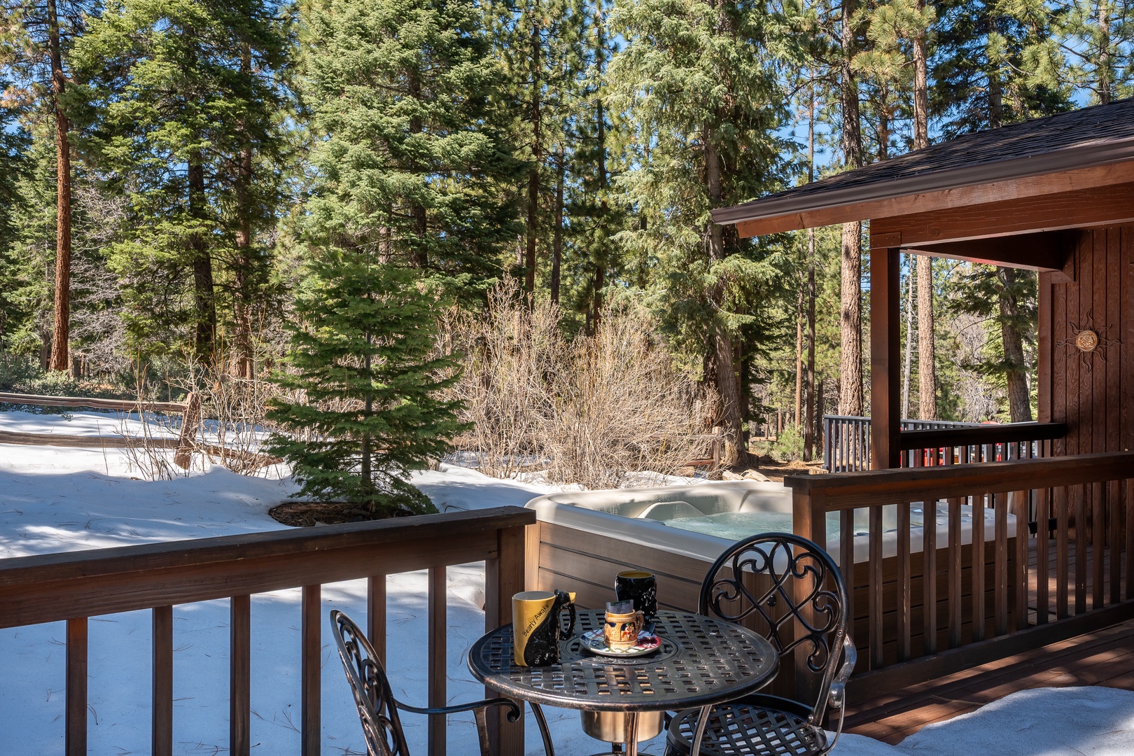 This private outdoor retreat overlooks a peaceful winter forest, offering a cozy spot for morning coffee with views of towering pines and a sparkling hot tub just steps away.