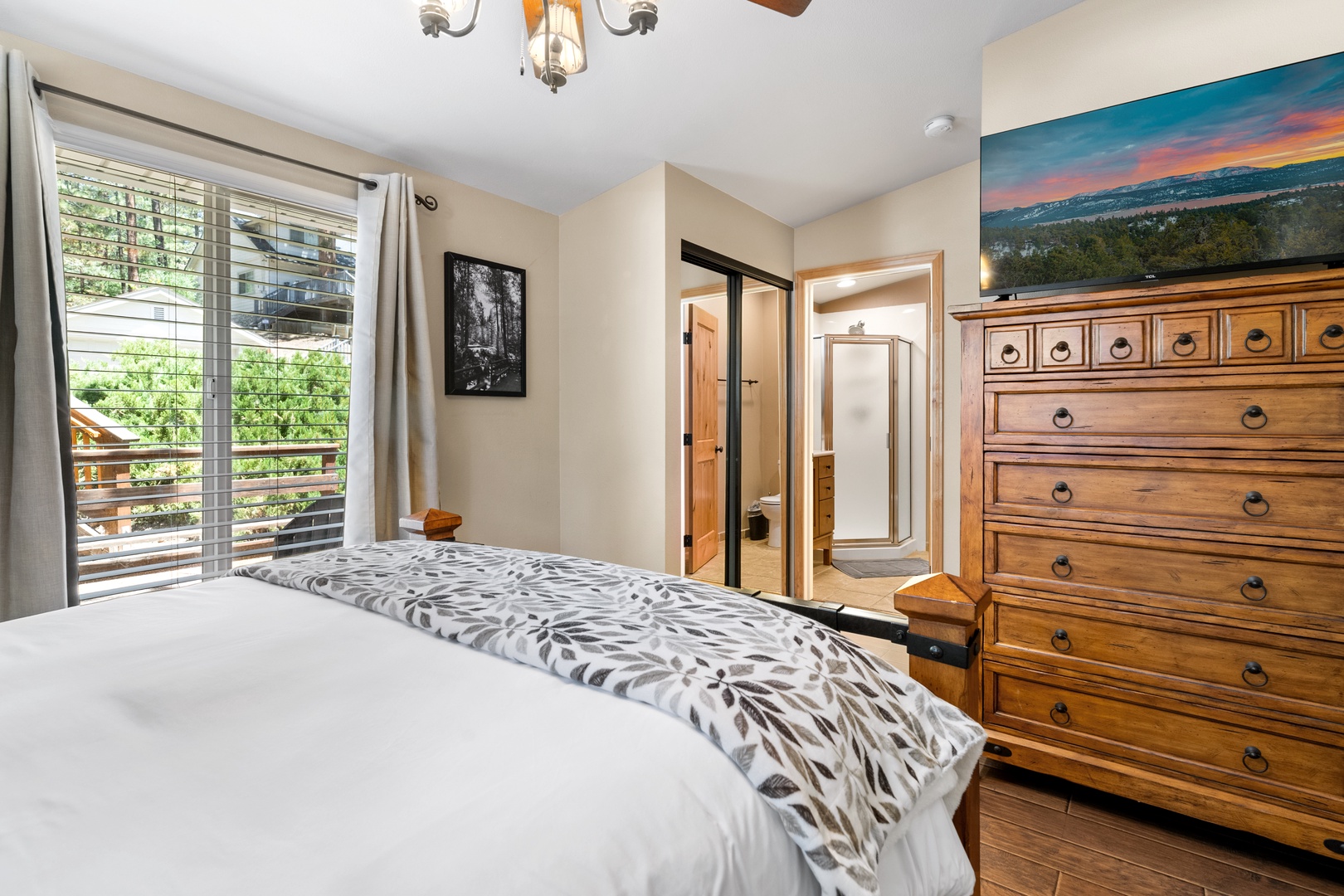 Wake up in this inviting bedroom with sunlight streaming through plantation shutters, showcasing a plush bed, handcrafted dresser, and artwork that brings the outdoors in—your peaceful mountain retreat awaits.