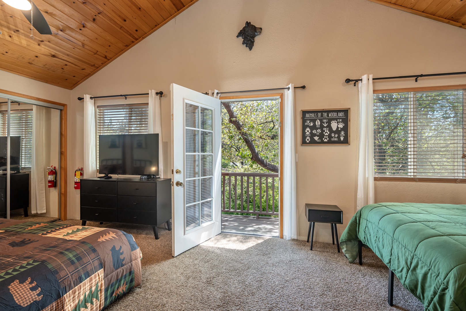 Your bright woodland-view bedroom opens onto a private deck where sunlight filters through the trees. Cozy beds and vaulted wood ceilings create a peaceful mountain retreat.