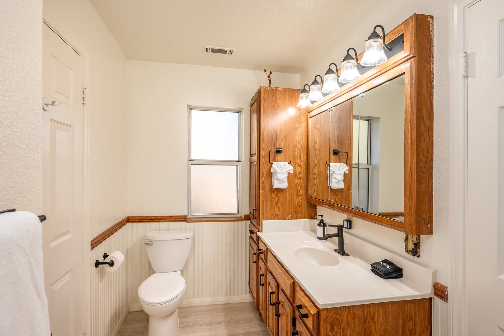 Your bright bathroom features warm wood vanity, double sinks, and classic beadboard wainscoting for a welcoming, rustic charm.