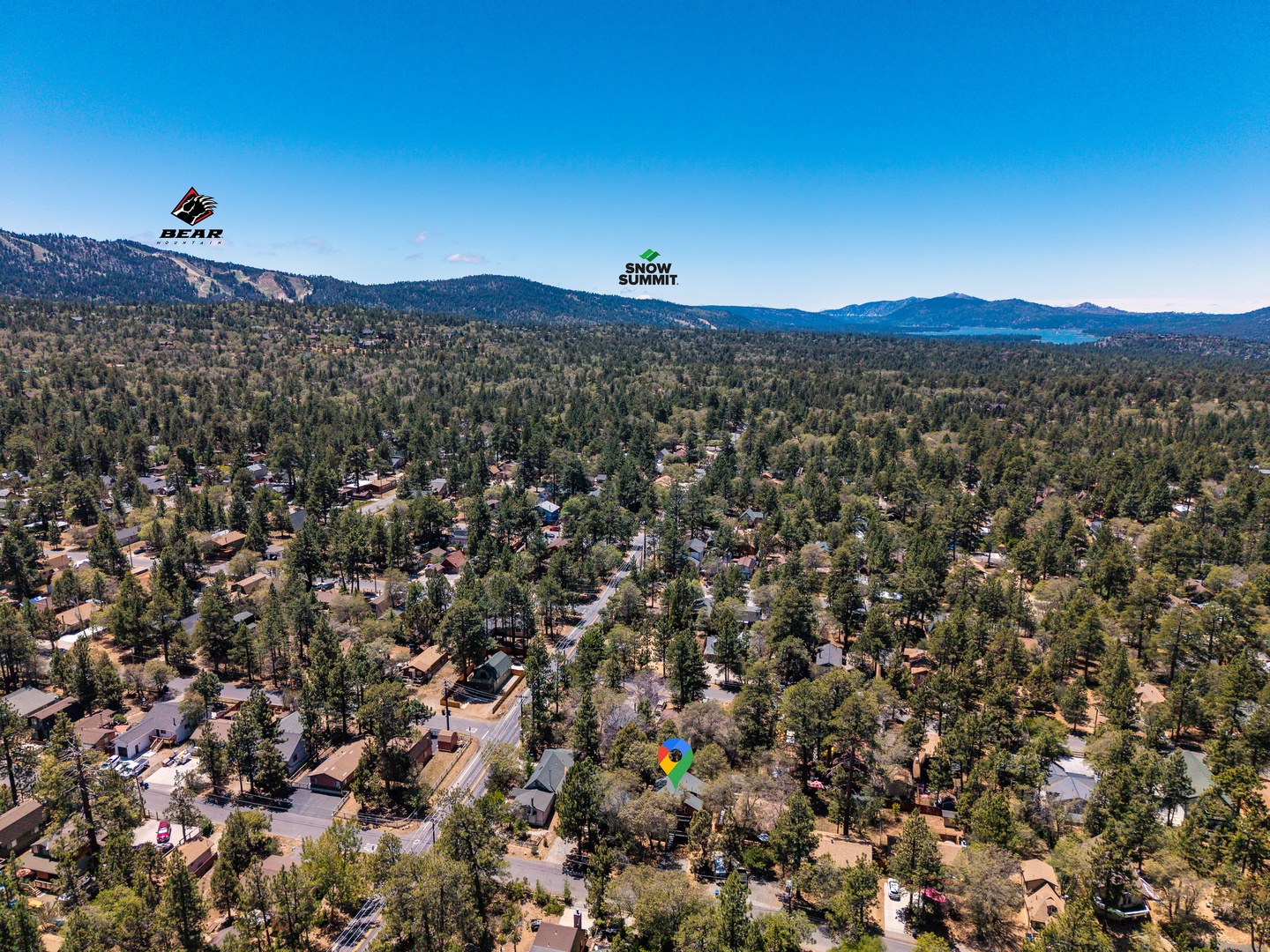 Aerial view of a mountain resort neighborhood nestled among towering pines, with Bear Mountain and Snow Summit ski areas marking the horizon.