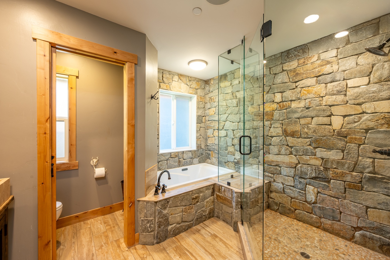 Your private spa retreat features a stunning stone-walled shower and soaking tub. Natural light and wood accents invite you to unwind.