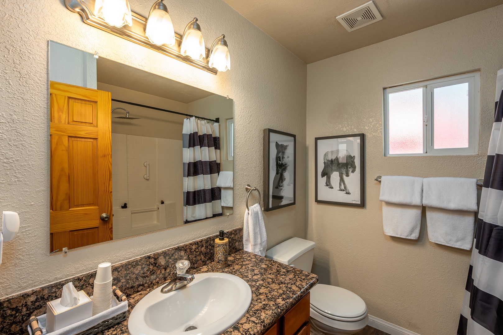 Your private bathroom features a granite vanity, well-lit mirror, and a tub-shower combo, all thoughtfully styled with fresh towels and cheerful artwork to help you feel right at home.