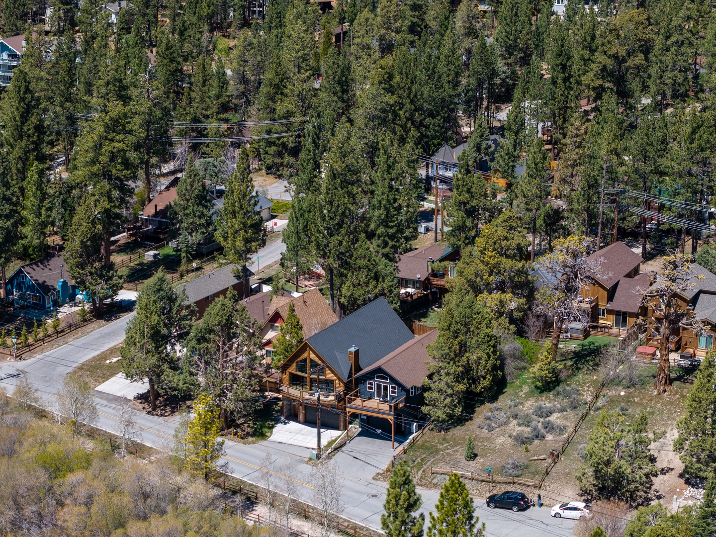 Aerial view of a charming mountain cabin retreat nestled among towering pines in a peaceful forested neighborhood, offering privacy and natural beauty.