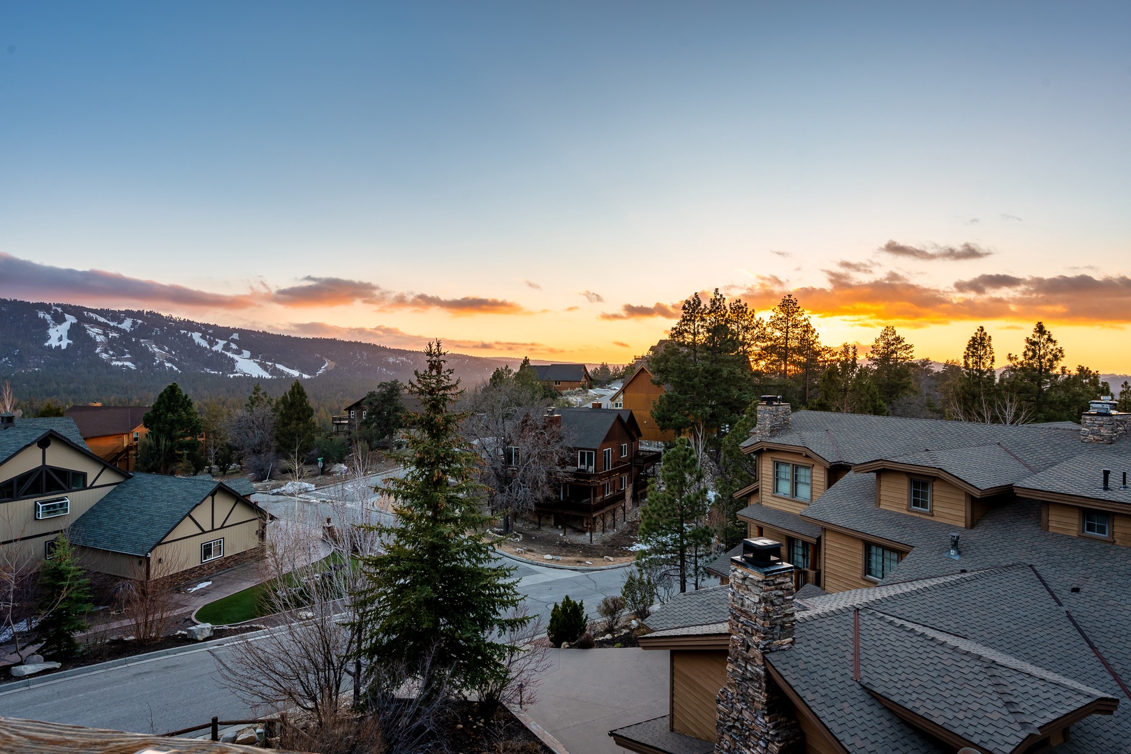 Mountain community at golden hour with ski slopes and forested hills creating a stunning backdrop for the residential neighborhood below.