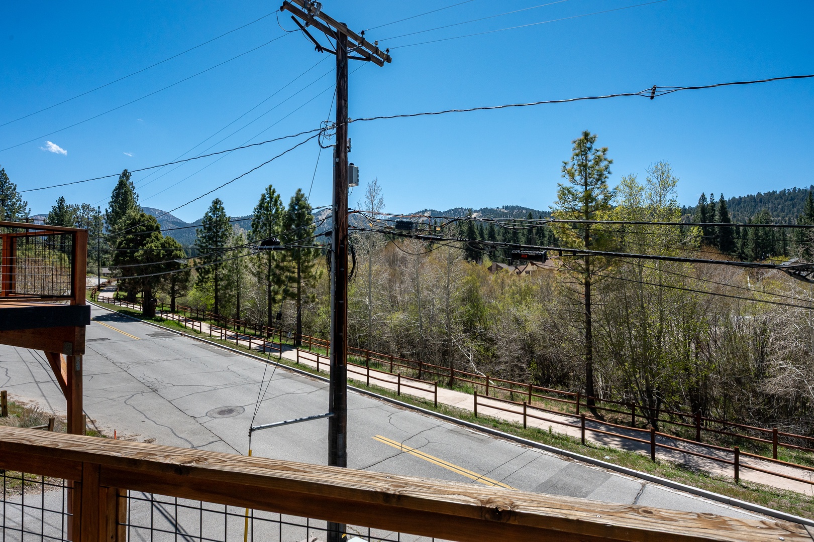 Mountain landscape view from property balcony overlooking wooded hillsides and a quiet residential street, with seasonal spring foliage beginning to bloom.