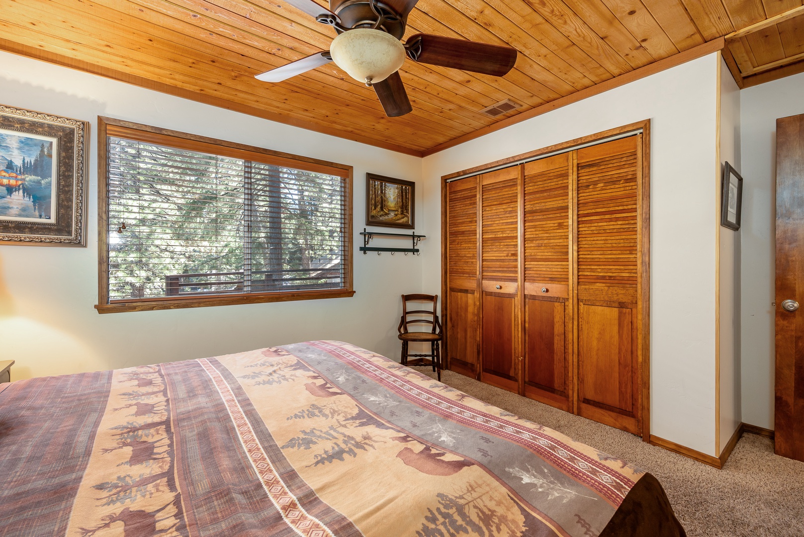 Your serene bedroom features a warm wood-paneled ceiling, soft natural light filtering through large windows, and a ceiling fan for your comfort. Generous closet space ensures you can unpack and settle in completely.