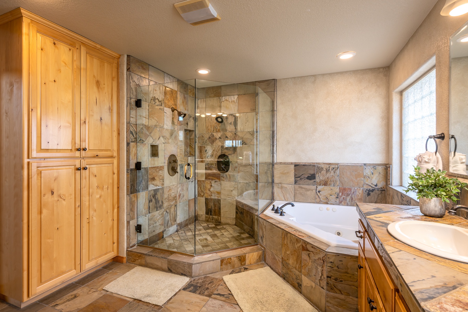 Indulge in your private spa-like retreat with heated stone floors, a luxurious soaking tub, and glass-enclosed shower featuring natural stone tilework.