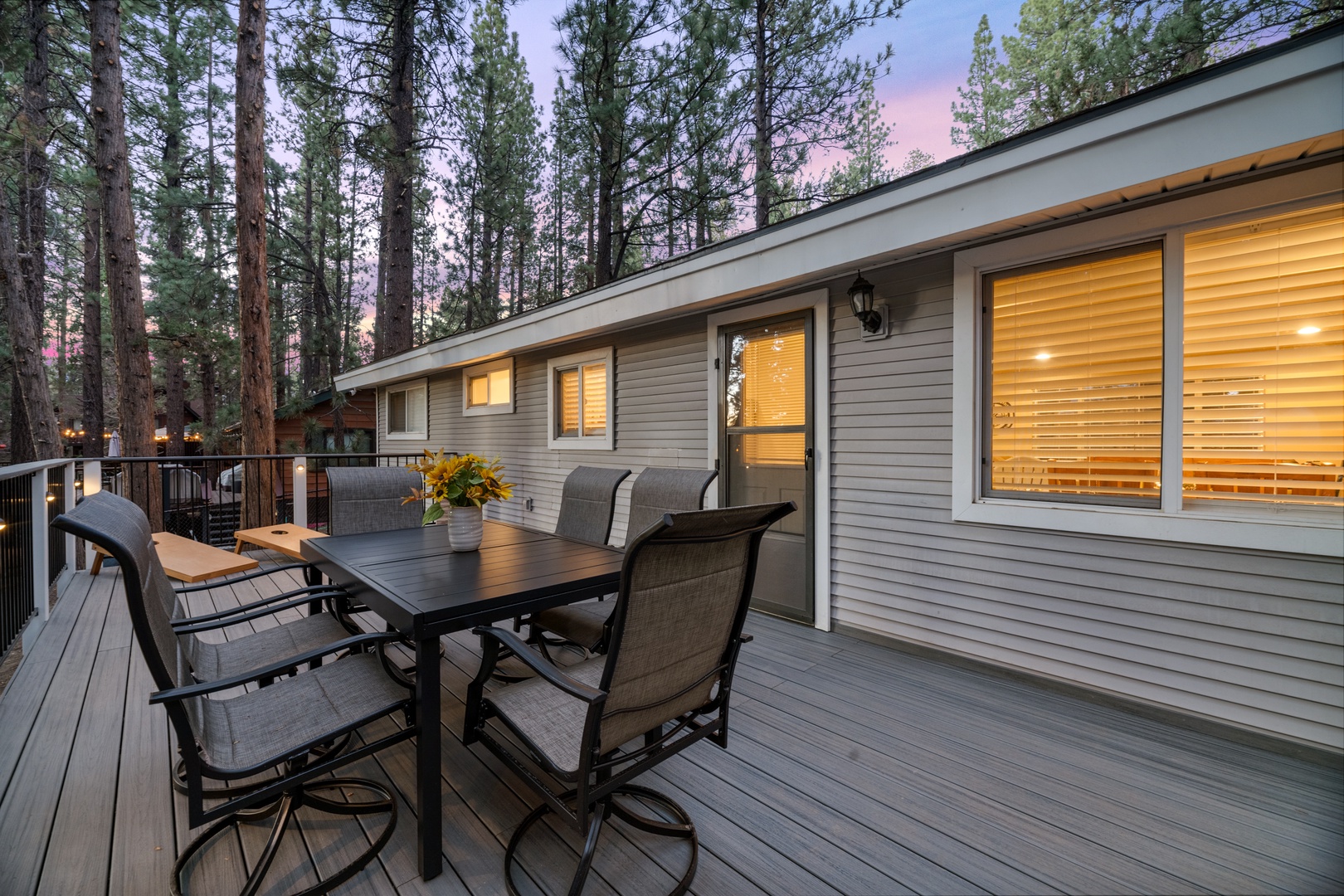 Nestled among towering pines, this spacious deck invites you to dine al fresco as twilight paints the sky. The warm glow from inside and forest backdrop create your perfect mountain retreat.