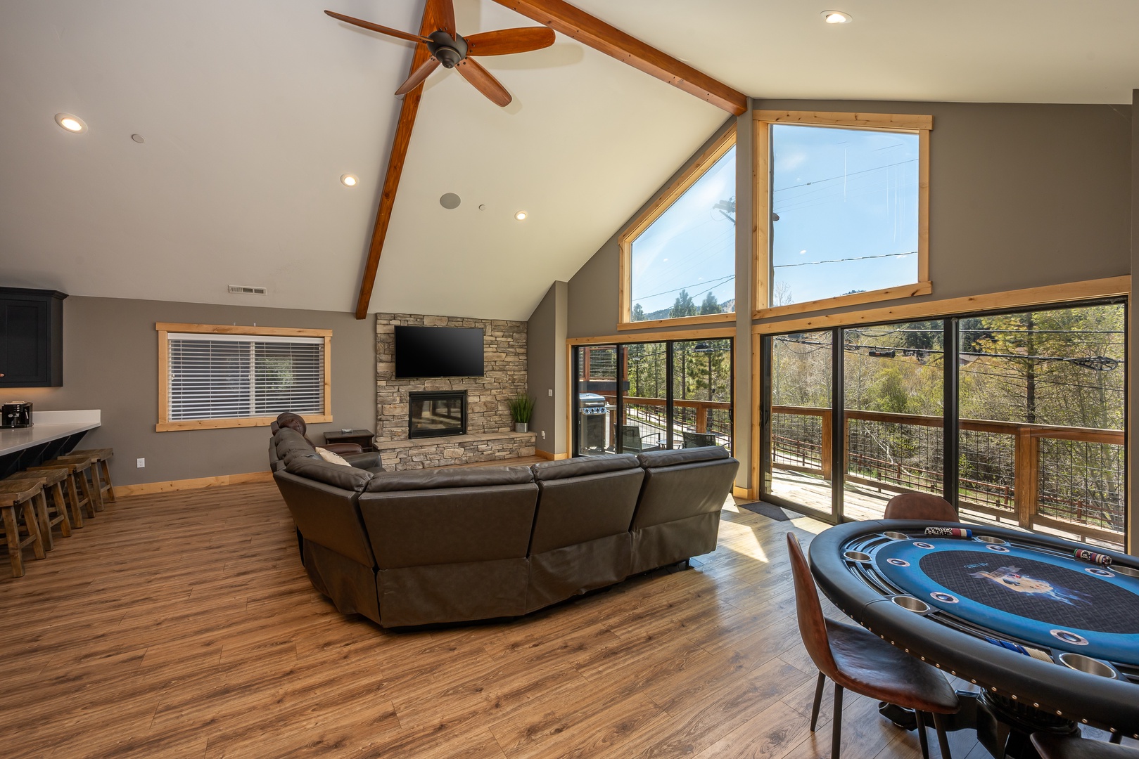 Your living space features soaring vaulted ceilings with warm wood beams, a cozy stone fireplace, and floor-to-ceiling windows framing peaceful forest views—ideal for relaxing or gathering with loved ones.
