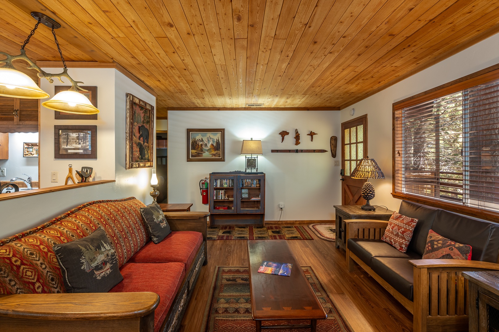 Relax in your cozy living room with vaulted wood ceilings, comfortable seating, rustic décor, and warm natural light streaming through large windows—your perfect mountain retreat awaits.