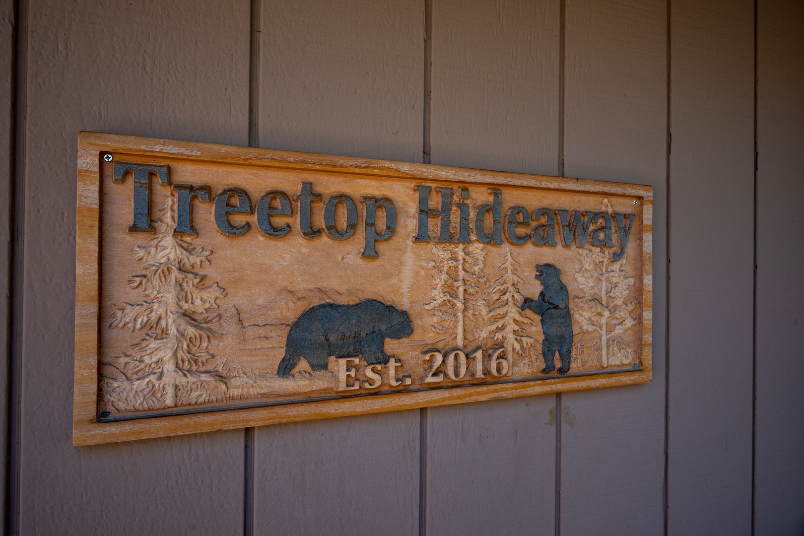 Hand-carved wooden entrance sign for Treetop Hideaway vacation rental, established 2016, featuring forest wildlife and mountain scenery.