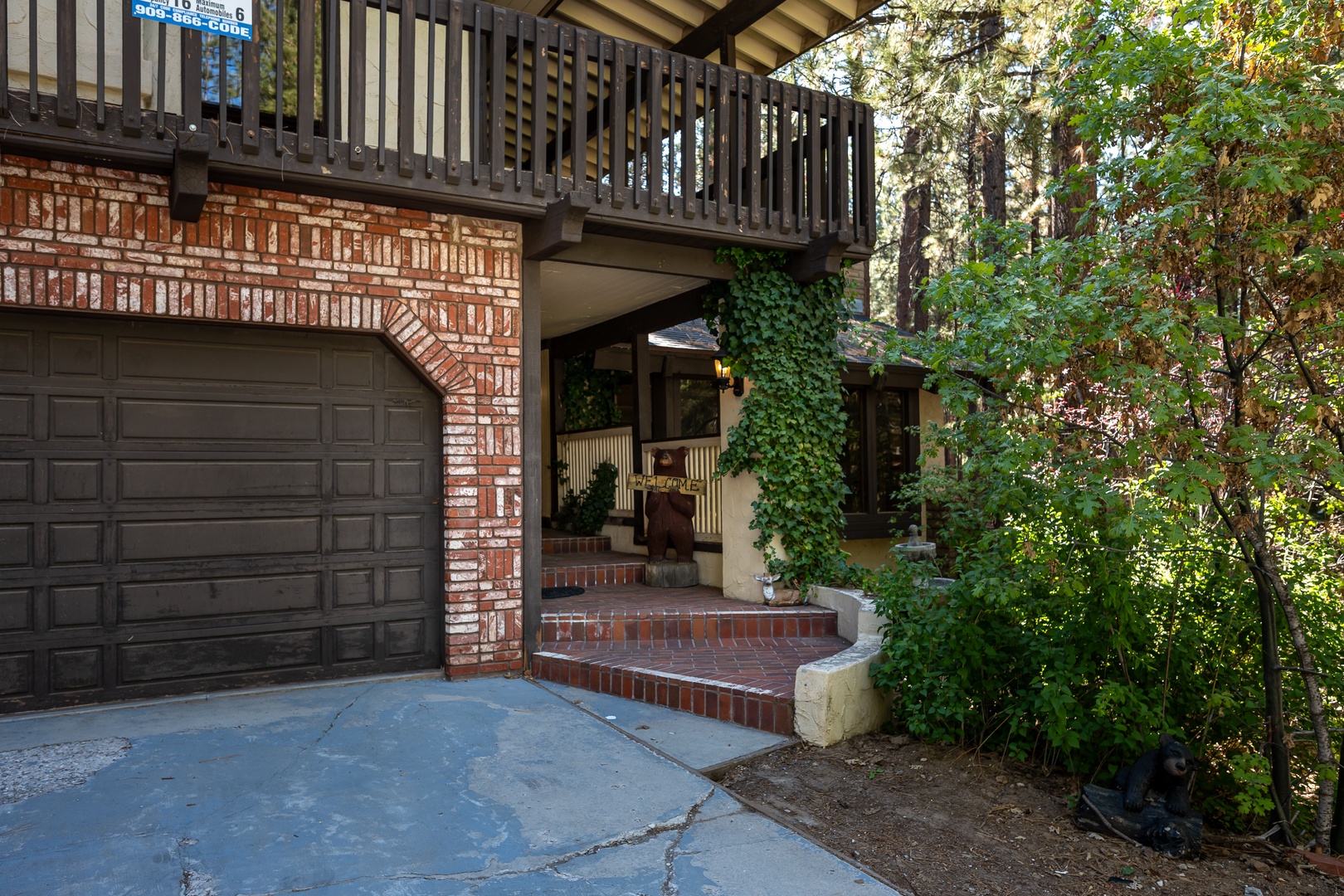Charming two-story property featuring brick and wood construction with private garage parking and an upper-level balcony, nestled among tall pines and natural greenery.