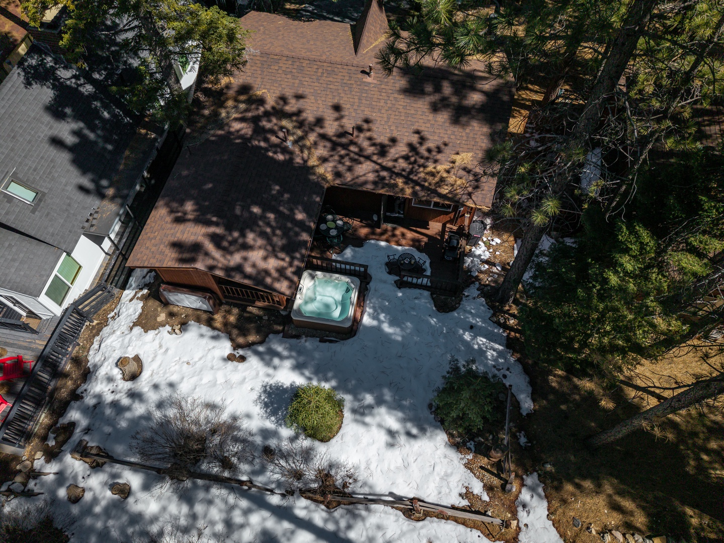 Aerial view of the property featuring a winter landscape with hot tub, deck areas, and mature trees surrounding the home.