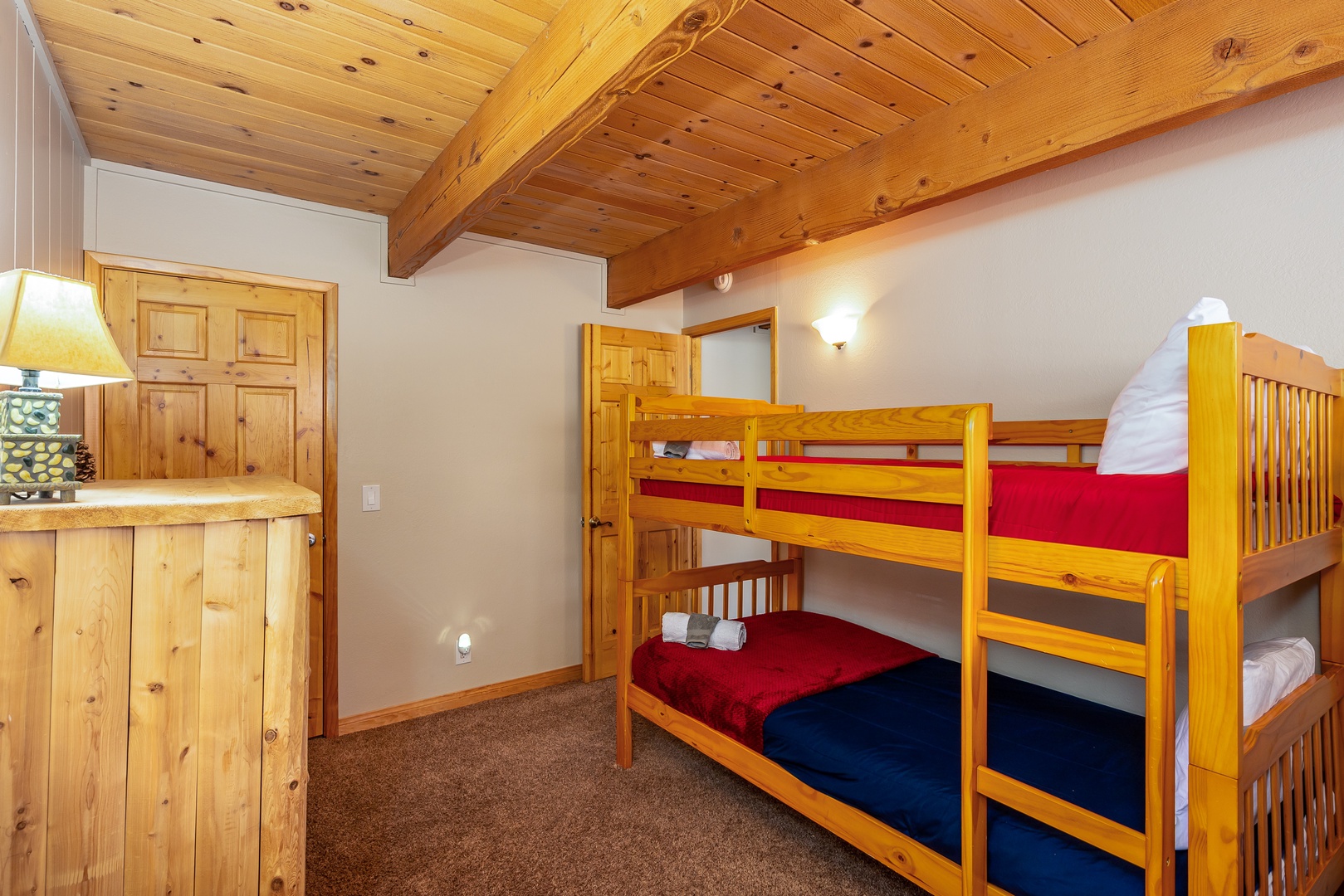 Your cozy mountain retreat features rustic wooden bunk beds with vibrant red and blue bedding, perfect for family adventures.