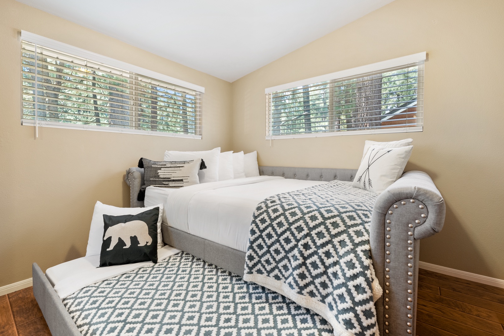 Wake up refreshed in this cozy bedroom featuring plush bedding, stylish gray upholstery, and bright windows that frame peaceful natural views. Your comfortable retreat awaits.