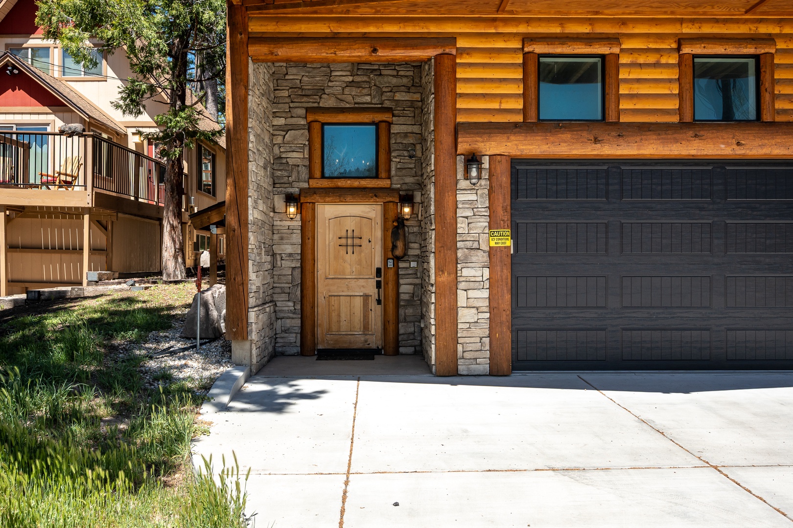 Charming mountain-style cabin featuring warm wood siding, stone accents, and a welcoming entrance, with convenient attached garage and private outdoor space for your stay.