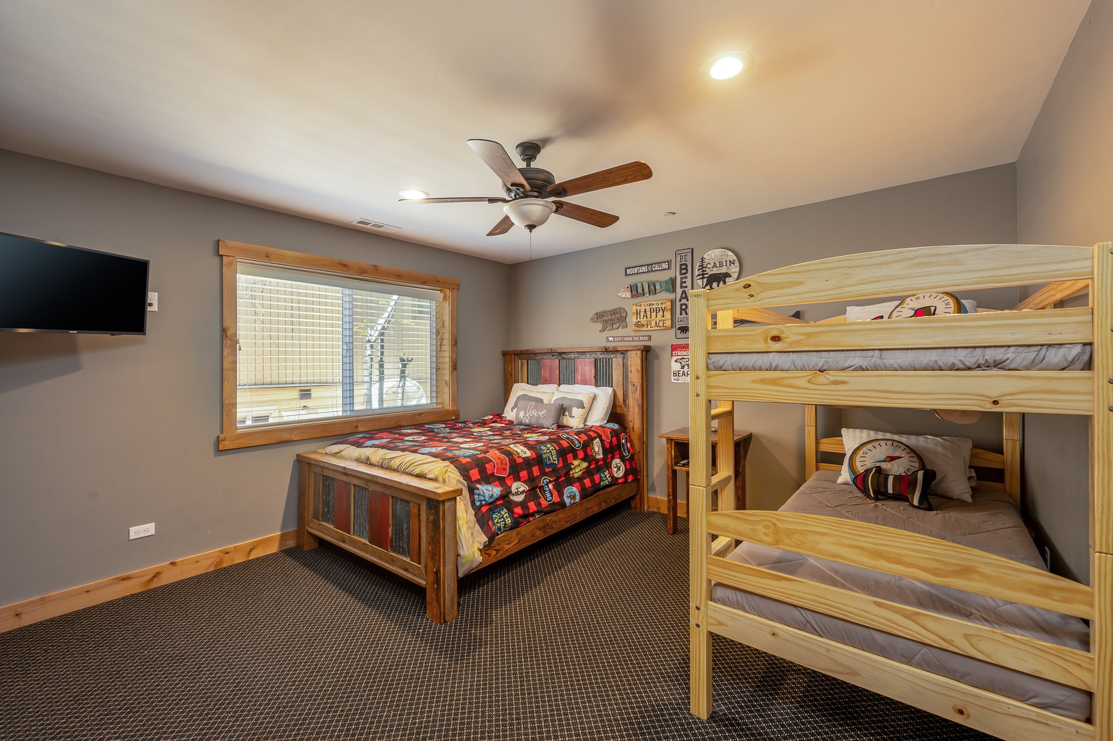 Your group will love this cozy cabin-themed bedroom with rustic wooden beds and a plush queen, all kept comfortable by a ceiling fan and plenty of natural light from the large window.