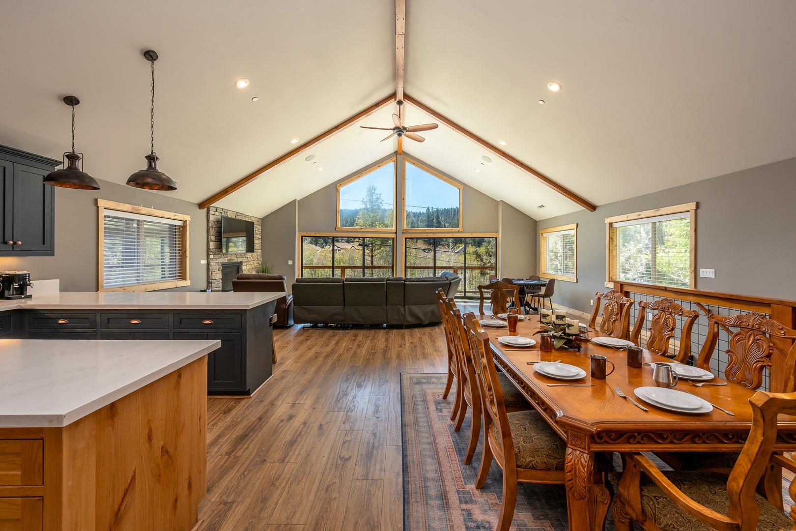 Soaring vaulted ceilings frame stunning forest views in this open-concept great room, where you can gather around the expansive dining table, relax by the fireplace, or prepare meals in the modern kitchen with ease.