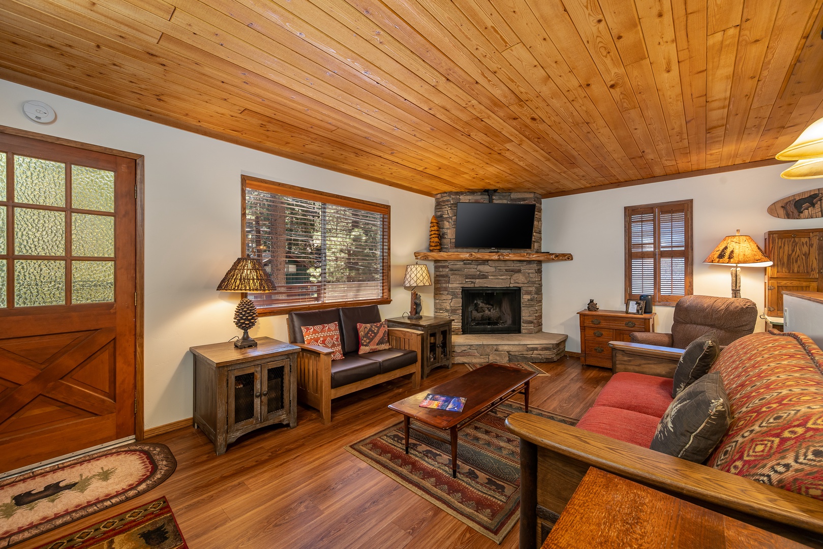 Picture yourself relaxing in this cozy living room with warm wood ceilings and a rustic stone fireplace. Sink into plush seating, enjoy your favorite shows, and let the inviting ambiance make you feel instantly at home.