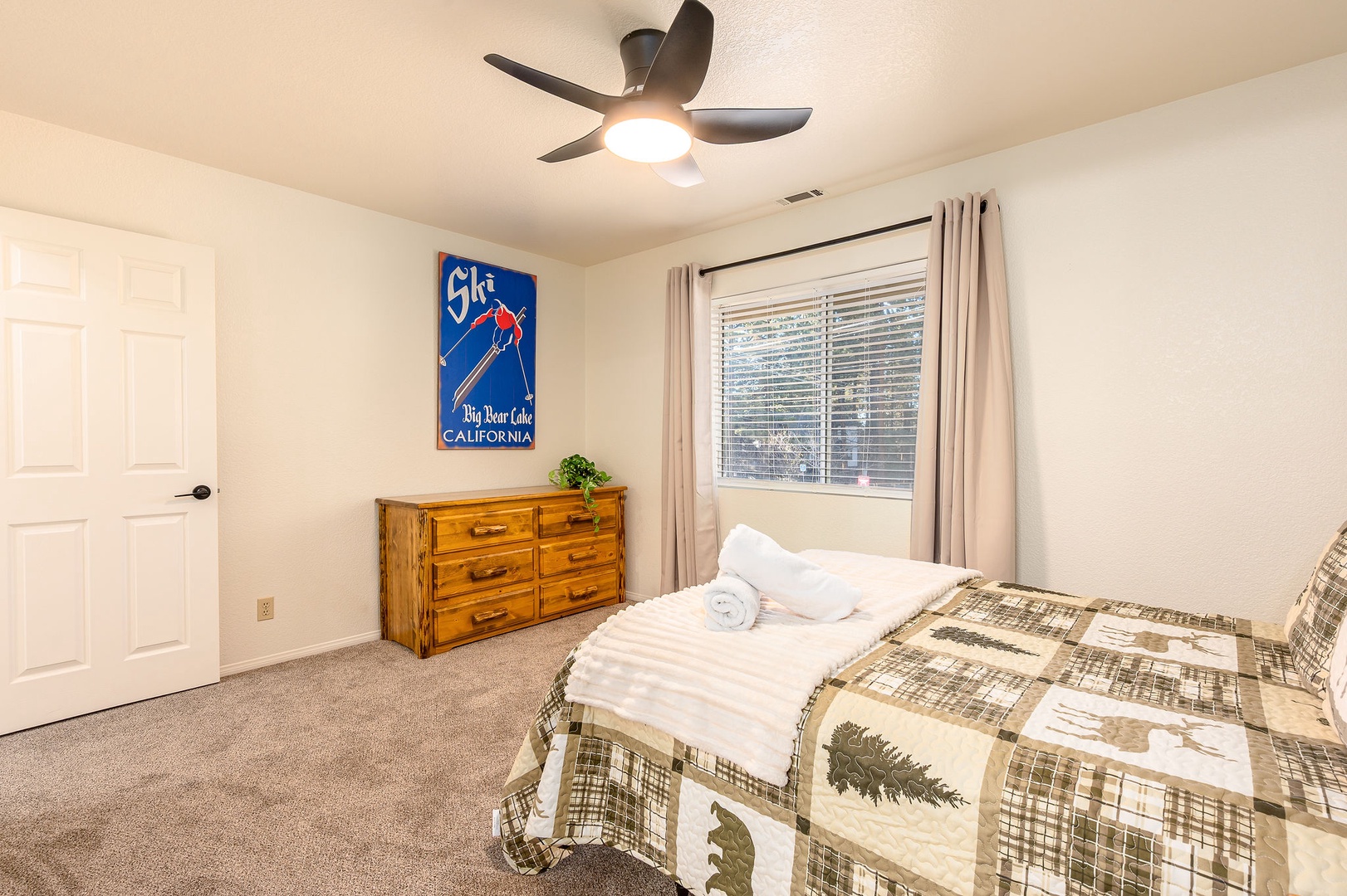 Relax in this comfortable bedroom featuring a cozy bed and wooden dresser for your belongings.