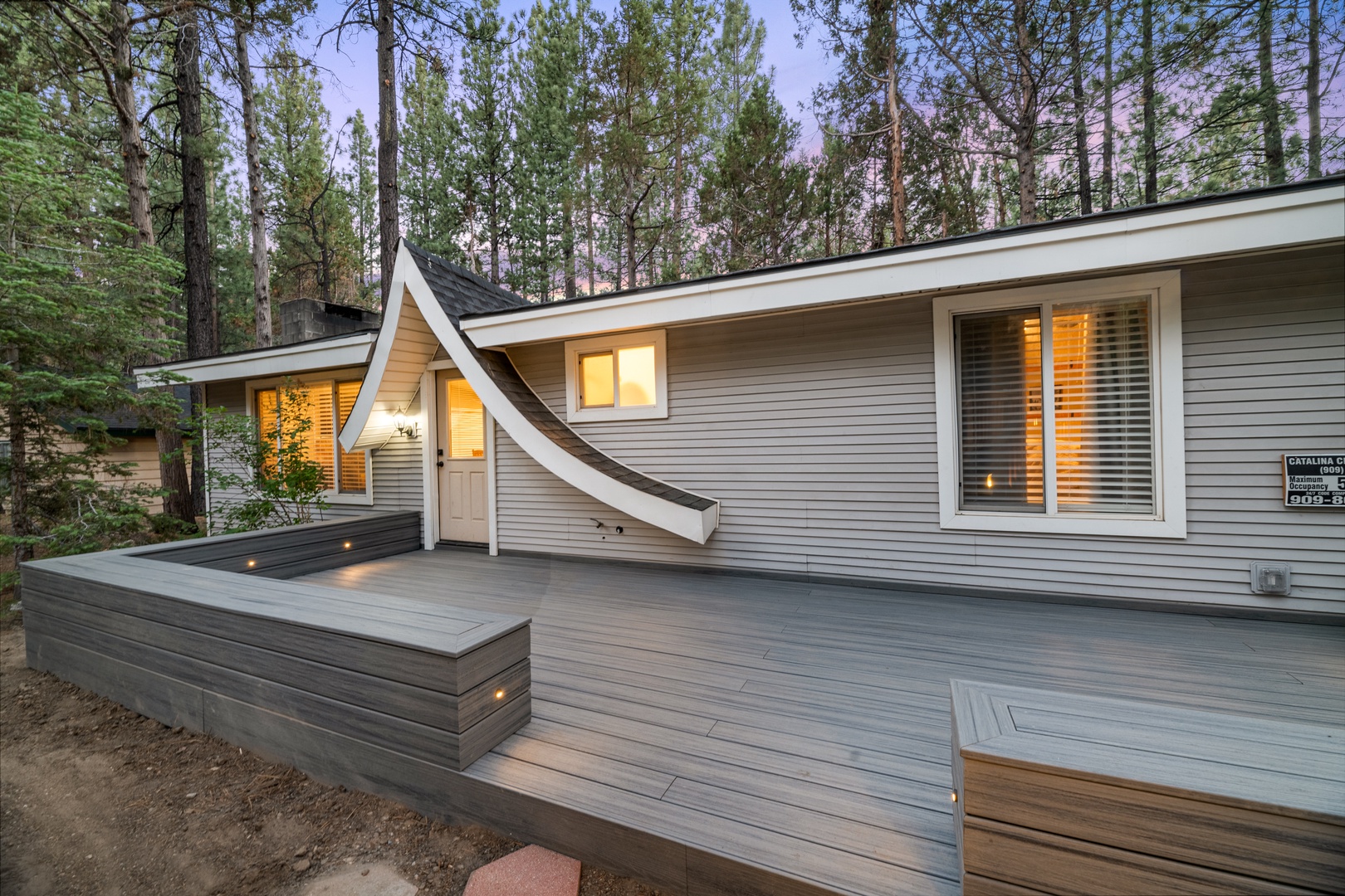 Nestled among towering pines, this modern cabin offers a spacious deck where you can unwind under a canopy of trees, with warm light welcoming you inside.