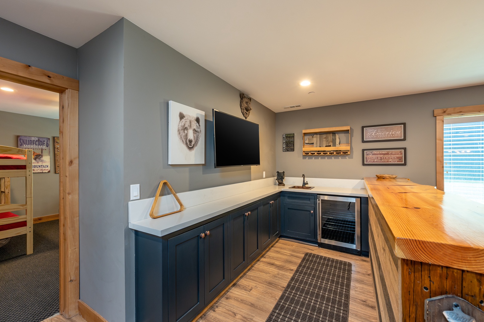 Your entertainment hub features a sleek kitchenette with navy cabinetry, a beverage fridge, and a live-edge bar—perfect for game nights and après-ski cocktails.