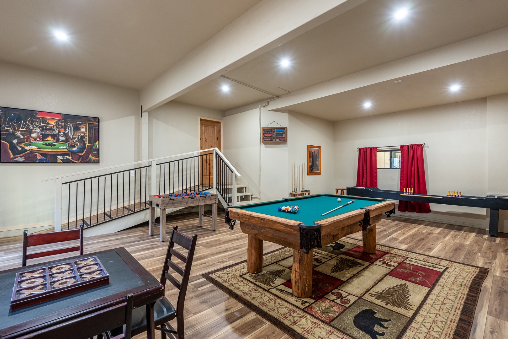 A spacious game room featuring a full-size pool table, arcade games, and dining area—perfect for friendly competition and entertainment. Natural light pours through large windows, highlighting polished hardwood floors and comfortable spaces to relax
