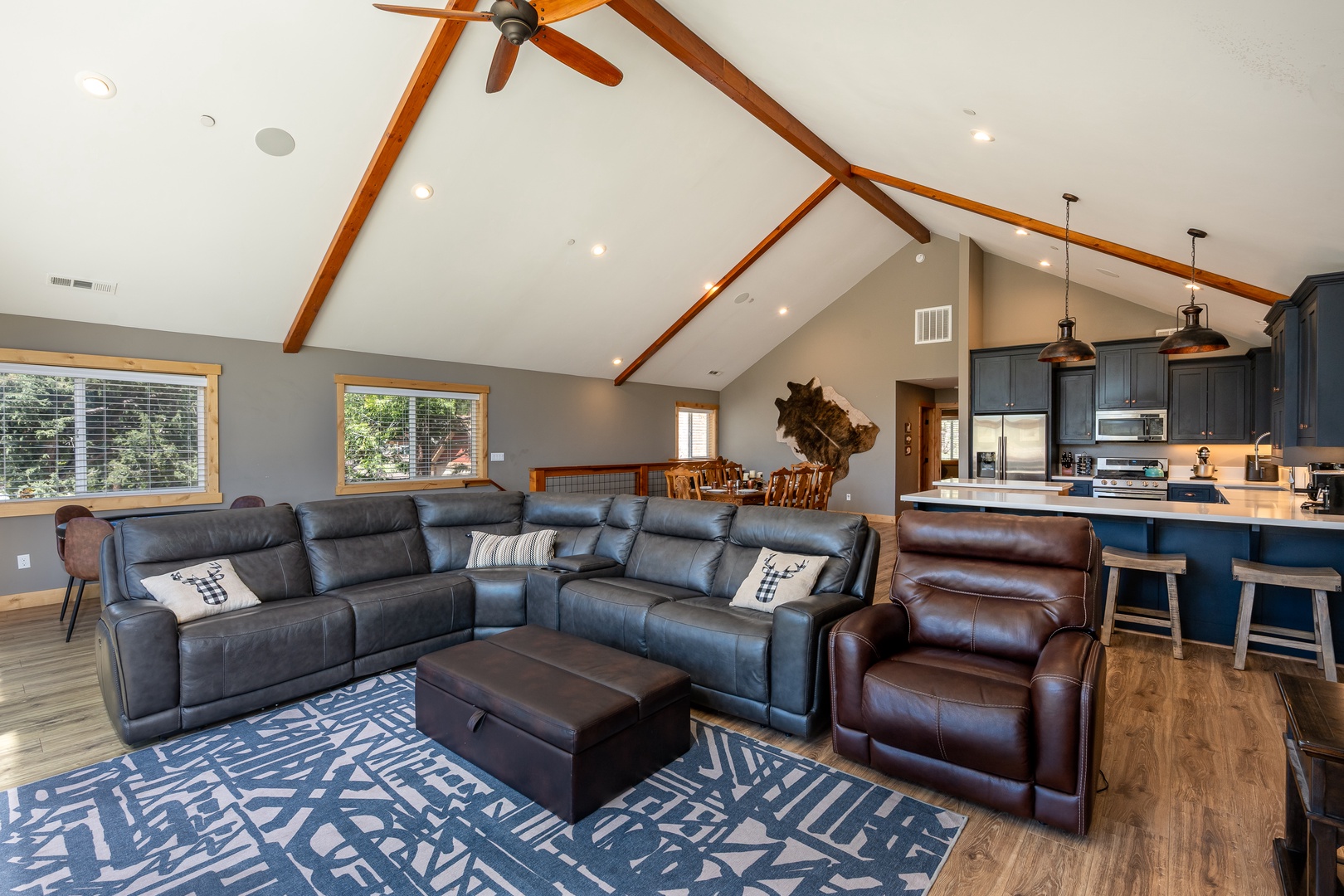 Relax in this expansive great room, under airy vaulted ceilings and striking wood beams. Sink into the reclining sectional, bathed in natural light.