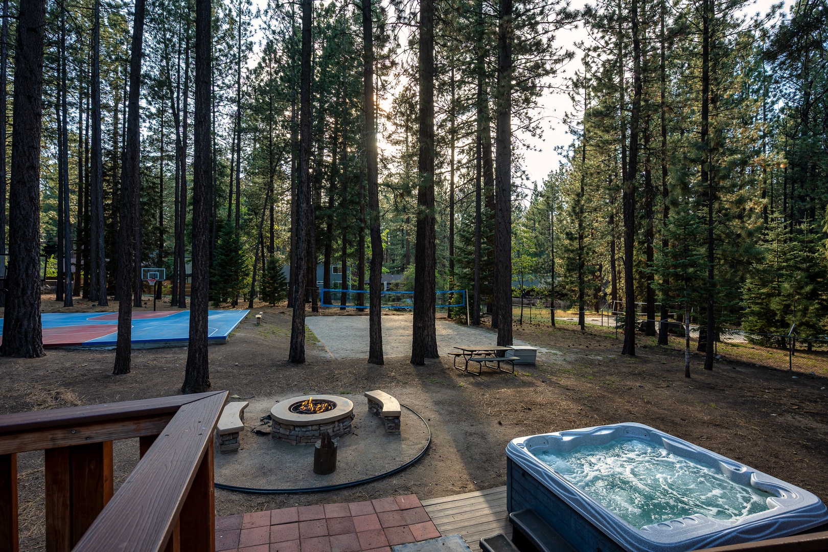 Scenic mountain property set among tall pines, featuring recreational amenities including a basketball court, fire pit, and hot tub in a peaceful forest setting.