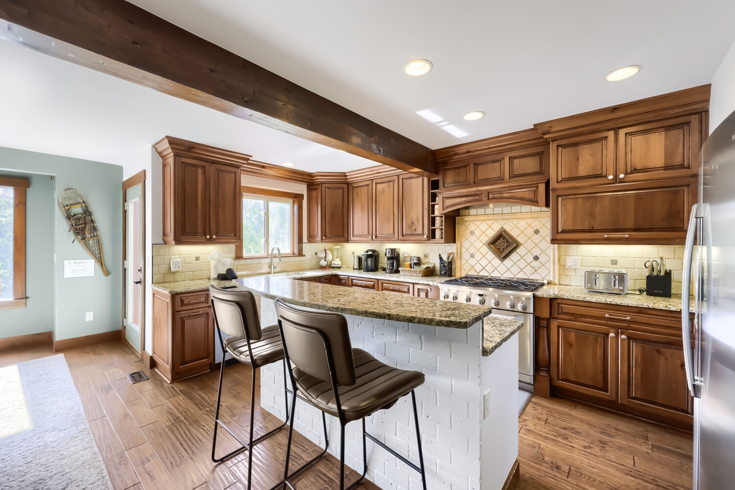 Your gourmet kitchen invites you to gather around the granite island, where rich wood cabinetry and modern appliances blend seamlessly beneath rustic beams and soft lighting—perfect for cooking and connecting.