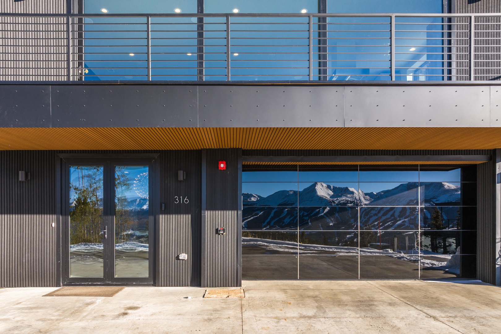 Modern property entrance features stunning mountain reflections in large glass windows, showcasing the area's natural beauty.
