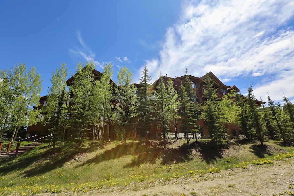 Mountain lodge nestled among towering aspens and pines under expansive blue skies with dramatic cloud formations.