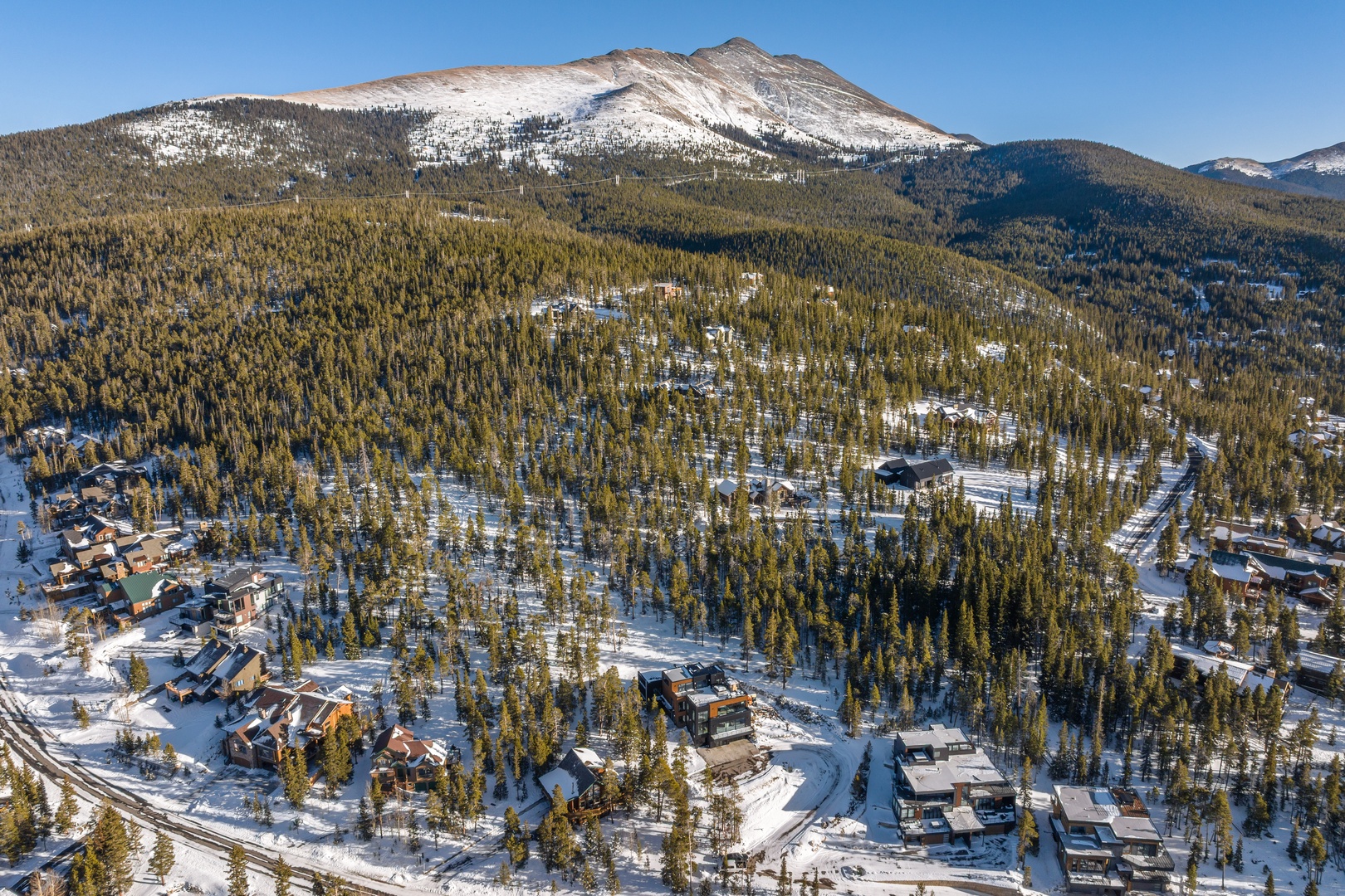 Aerial view of a mountain community nestled among snow-covered forests with dramatic peaks rising in the background.