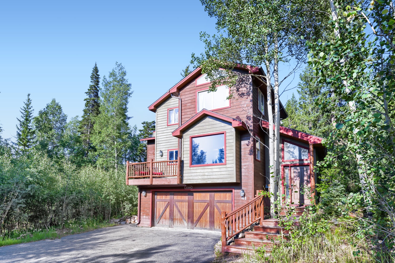 A charming mountain home framed by leafy birch and evergreen trees, featuring warm wood tones and a private balcony—your peaceful escape in a natural setting.