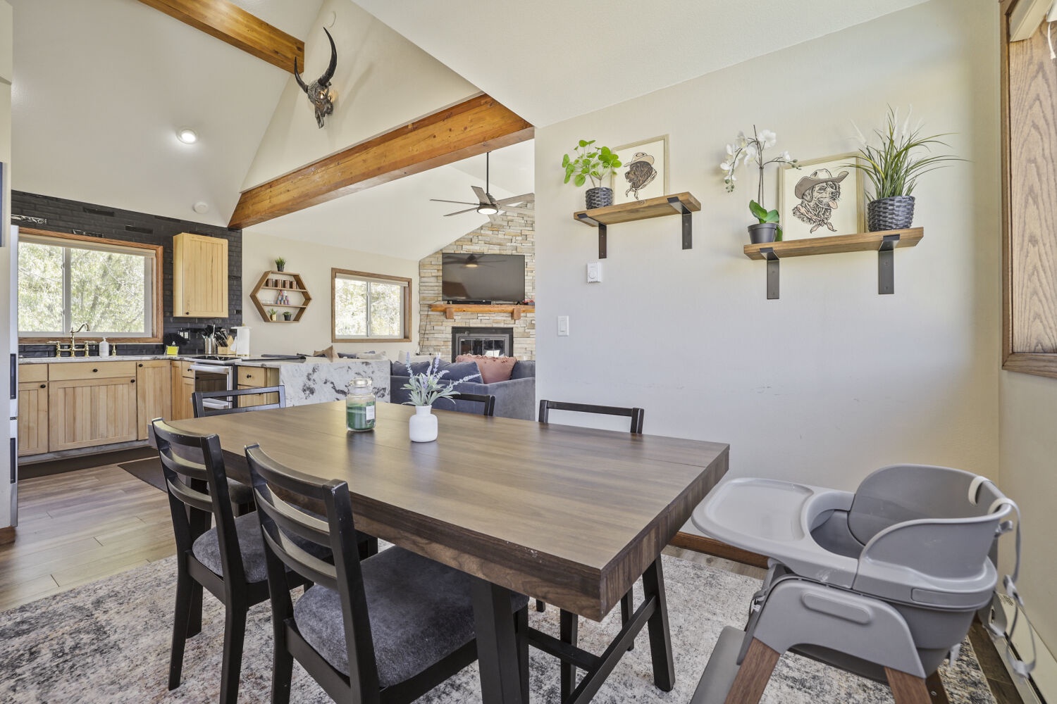 Gather around the dining table in this light-filled open space, where exposed wooden beams and a cozy stone fireplace create the perfect backdrop for your mountain retreat meals and memorable conversations.