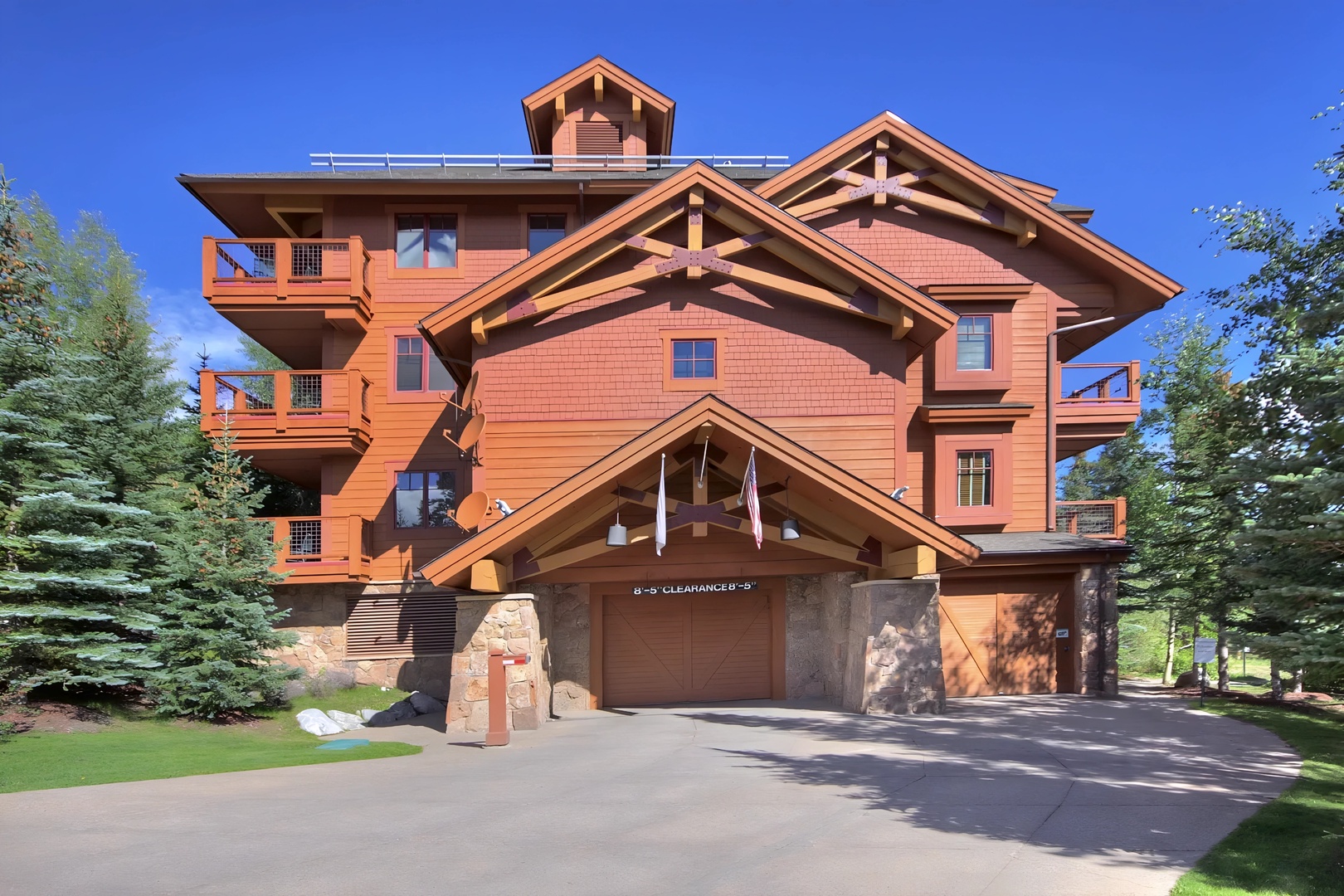 Striking mountain lodge with distinctive timber architecture and stone accents, featuring covered garage and mature landscaping against vibrant blue skies.